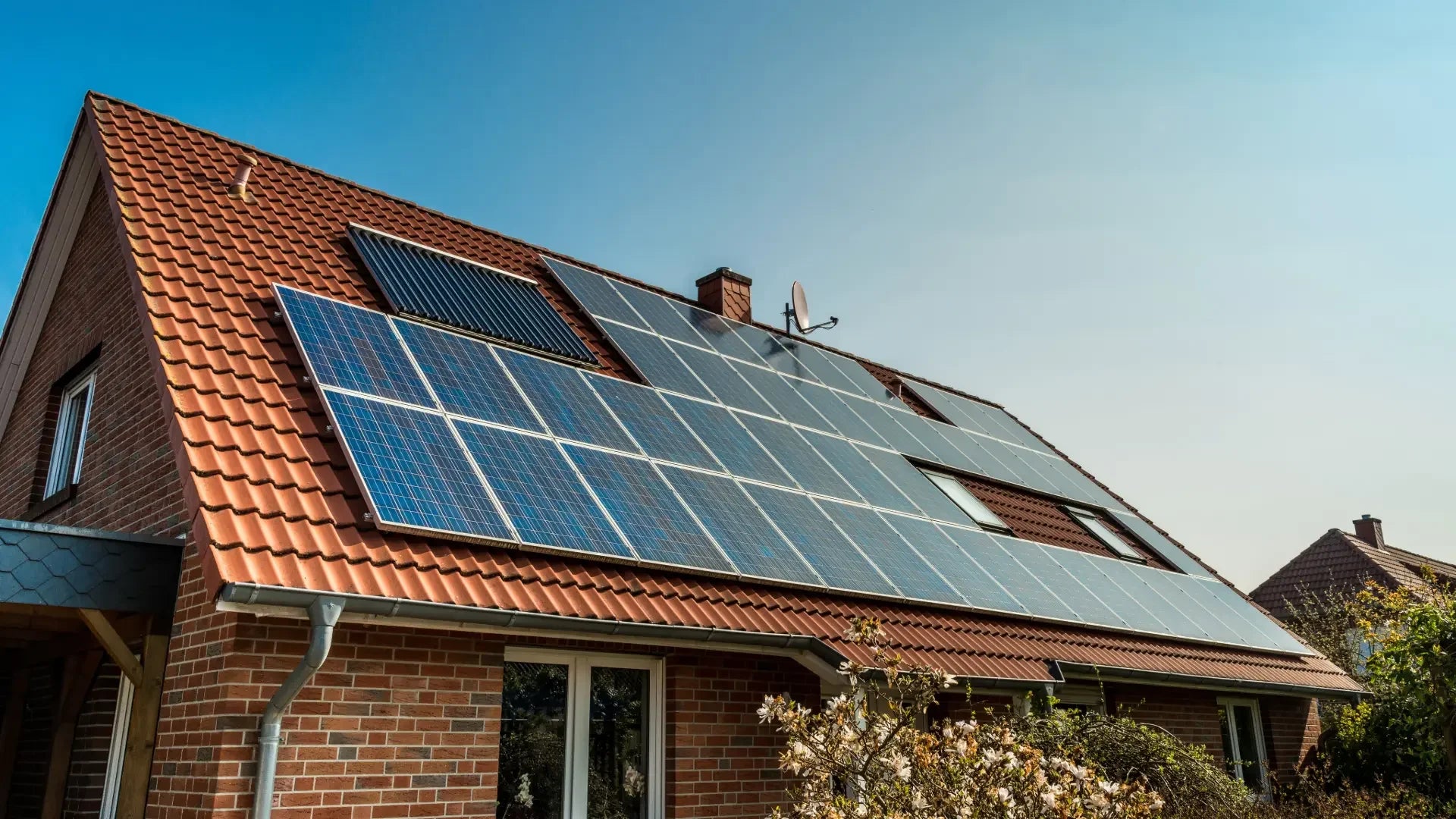 Solaranlage auf Dach eines Hauses mit roten Ziegeln und blauem Himmel